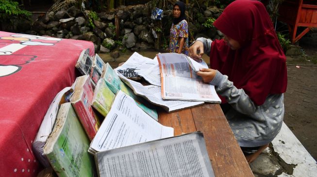 Seorang pelajar SMA menjemur buku pelajaran yang sebelumya terendam banjir di Kabupaten Madiun, Jawa Timur, Kamis (20/1/2022). ANTARA FOTO/Siswowidodo