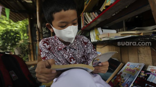 Seorang anak membaca buku di pustaka mini Bale Buku di Kelurahan Dukuh, Kramat Jati, Jakarta, Kamis (20/1/2022). [Suara.com/Angga Budhiyanto]