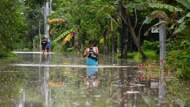 Warga menerobos jalan yang terendam banjir di Kabupaten Madiun, Jawa Timur, Kamis (20/1/2022). ANTARA FOTO/Siswowidodo
