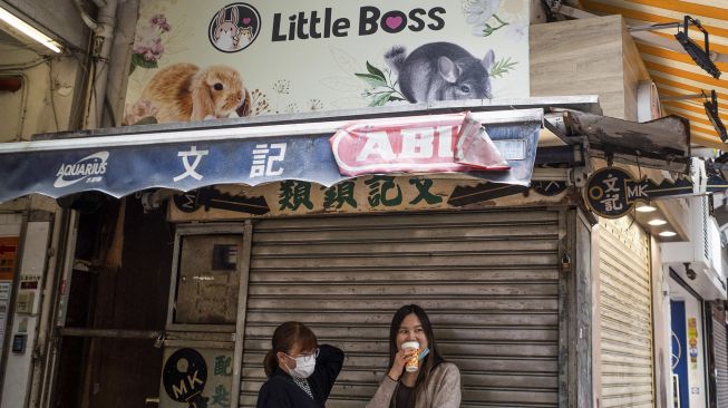 Orang-orang berdiri di bawah spanduk toko hewan peliharaan di mana seorang karyawan dan pelanggan kemudian dinyatakan positif COVID-19 setelah menangani hamster, di Causeway Bay, Hong Kong, pada (18/1/2022). [BERTHA WANG / AFP]