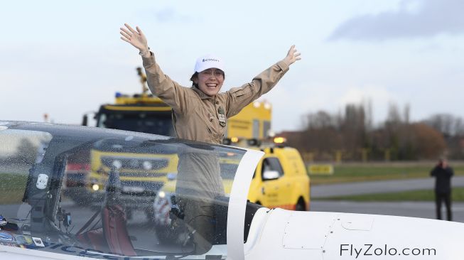 Pilot remaja Belgia-Inggris Zara Rutherford berdiri di atas pesawat Ultralight Shark setelah mendarat kembali di akhir perjalanan solo keliling dunianya di Kota Kortrijk, Belgia, pada (20/1/2022). [JOHN THYS / AFP]