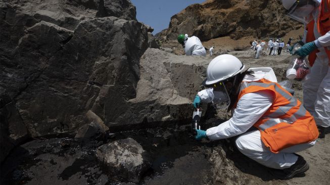 Petugas membersihkan tumpahan minyak dari pantai di Provinsi Callao, Peru, pada (17/1/2022). [CRIS BOURONCLE / AFP]