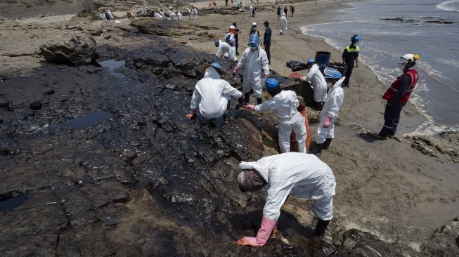 Petugas membersihkan tumpahan minyak dari pantai di Provinsi Callao, Peru, pada (17/1/2022). [CRIS BOURONCLE / AFP]