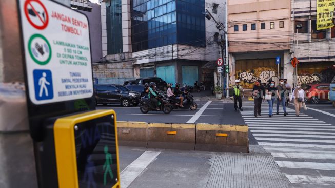 Warga menyeberang melalui pelican crossing di Kawasan Glodok, Jakarta Barat, Minggu (23/1/2022). [Suara.com/Alfian Winanto]