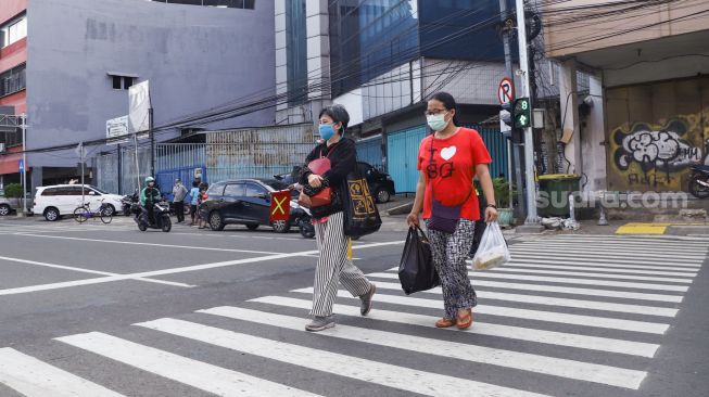 Warga menyeberang melalui pelican crossing di Kawasan Glodok, Jakarta Barat, Minggu (23/1/2022). [Suara.com/Alfian Winanto]