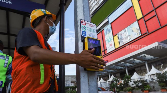 Petugas menekan alat untuk menyeberang melalui pelican crossing di Kawasan Glodok, Jakarta Barat, Minggu (23/1/2022). [Suara.com/Alfian Winanto]