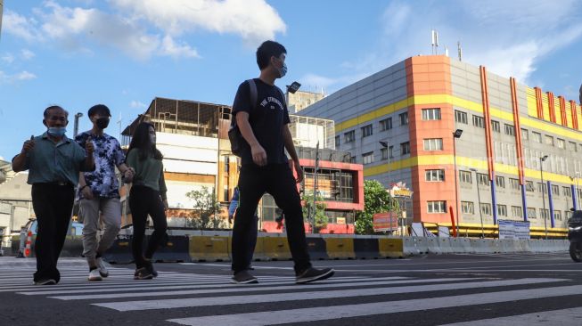 Warga menyeberang melalui pelican crossing di Kawasan Glodok, Jakarta Barat, Minggu (23/1/2022). [Suara.com/Alfian Winanto]