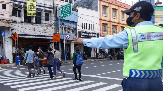 Petugas membantu warga menyeberang melalui pelican crossing di Kawasan Glodok, Jakarta Barat, Minggu (23/1/2022). [Suara.com/Alfian Winanto]