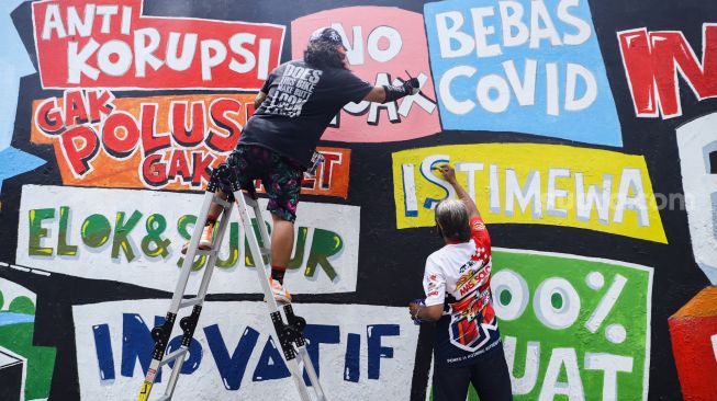 Pekerja seni membuat mural di kawasan Palmerah, Jakarta Pusat, Minggu (23/1/2022). [Suara.com/Alfian Winanto]