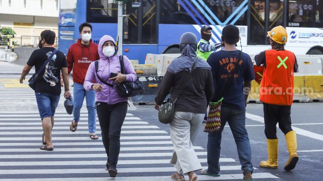 Warga menyeberang melalui pelican crossing di Kawasan Glodok, Jakarta Barat, Minggu (23/1/2022). [Suara.com/Alfian Winanto]