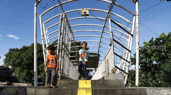 Anak-anak melintas di Jembatan Penyeberangan Orang (JPO) Jayakarta di Menteng, Jakarta Pusat, Senin (24/1/2022). [Suara.com/Alfian Winanto]