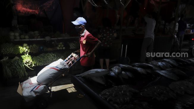 Buruh angkut berjalan di samping lapak ikan bandeng di kawasan Petak Sembilan, Glodok, Jakarta, Senin (24/1/2022). [Suara.com/Angga Budhiyanto]