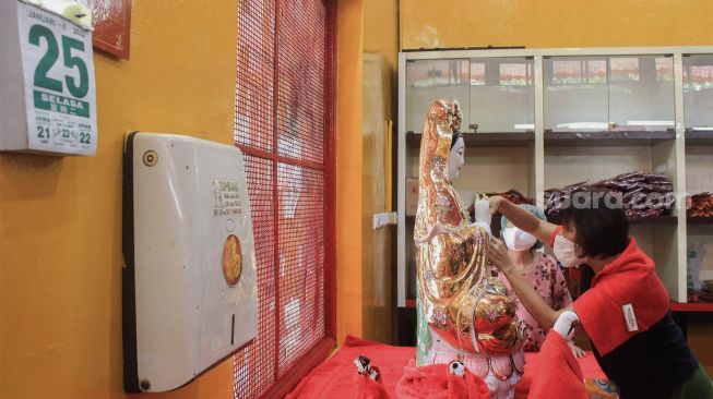 Petugas membersihkan patung dewa di Vihara Amurva Bhumi, Jakarta, Selasa (25/1/2022). [Suara.com/Septian]