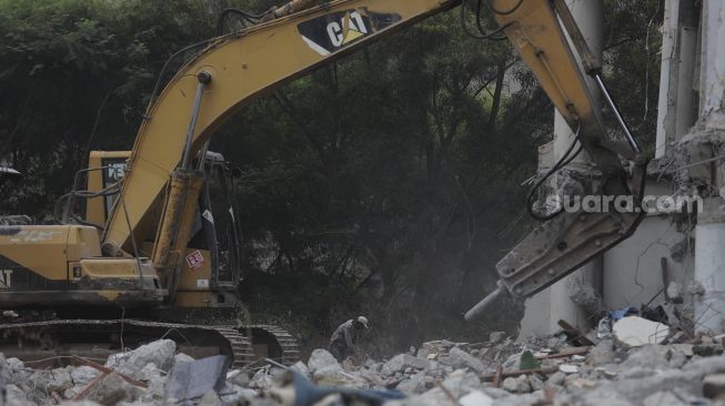 Pekerja dibantu alat berat menyelesaikan pengerjaan renovasi Museum Telekomunikasi di Taman Mini Indonesia Indah (TMII), Jakarta, Rabu (26/1/2022). [Suara.com/Angga Budhiyanto]