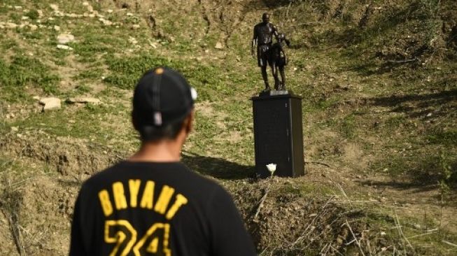 Seseorang melihat patung perunggu karya seniman Dan Medina, yang menggambarkan Kobe Bryant, putri Gianna Bryant, dan nama-nama mereka yang meninggal, selama peringatan sementara satu hari di lokasi kecelakaan helikopter 2020 di Calabasas, California, pada Januari 26 Januari 2022.  Patrick T. FALLON / AFP