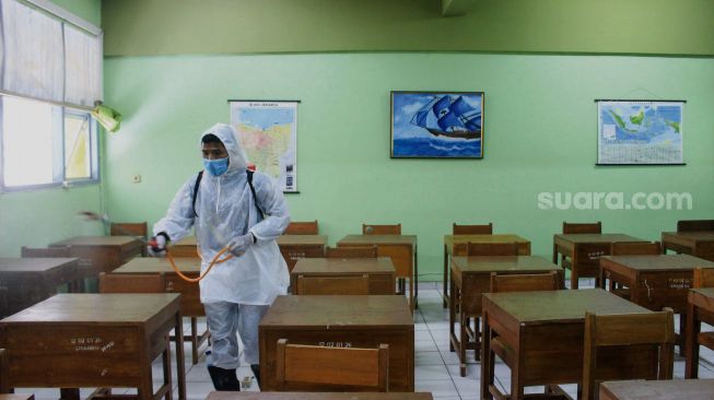 Petugas Palang Merah Indonesia (PMI) menyemprotkan cairan disinfektan di SMA Negeri 66 Jakarta, Jumat (28/1/2022). [Suara.com/Septian]