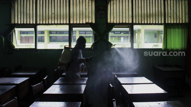 Petugas Palang Merah Indonesia (PMI) menyemprotkan cairan disinfektan di SMA Negeri 66 Jakarta, Jumat (28/1/2022). [Suara.com/Septian]