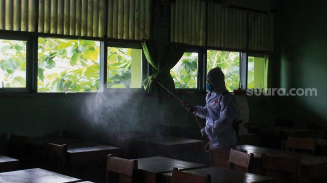 Petugas Palang Merah Indonesia (PMI) menyemprotkan cairan disinfektan di SMA Negeri 66 Jakarta, Jumat (28/1/2022). [Suara.com/Septian]