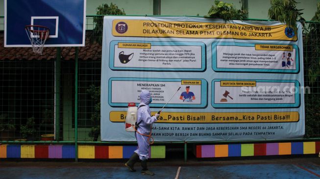 Petugas Palang Merah Indonesia (PMI) menyemprotkan cairan disinfektan di SMA Negeri 66 Jakarta, Jumat (28/1/2022). [Suara.com/Septian]