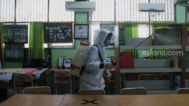 Petugas Palang Merah Indonesia (PMI) menyemprotkan cairan disinfektan di SMA Negeri 66 Jakarta, Jumat (28/1/2022). [Suara.com/Septian]