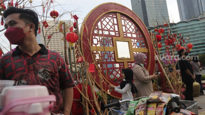 Warga berdiri di dekat ornamen dengan nuansa Imlek yang di pasang di sekitar Bundaran Hotel Indonesia (HI), Jakarta, Sabtu (29/1/2022). [Suara.com/Angga Budhiyanto]