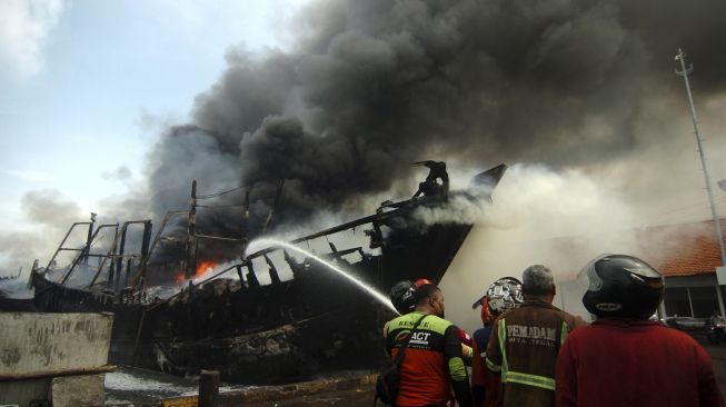 Petugas pemadam kebakaran menyemprotkan air pada kapal nelayan yang terbakar di Pelabuhan Tegal, Jawa Tengah, Sabtu (29/1/2022). [ANTARA FOTO/Oky Lukmansyah]