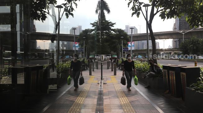 Pekerja berjalan di trotoar kawasan Sudirman, Jakarta, Rabu (2/2/2022). [Suara.com/Angga Budhiyanto]