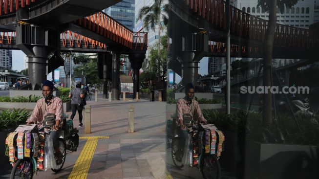 Pedagang keliling melintas di trotoar kawasan Sudirman, Jakarta, Rabu (2/2/2022). [Suara.com/Angga Budhiyanto]
