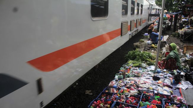 Kereta api melintas saat pedagang berjualan di pinggir rel kereta api di Surabaya, Jawa Timur, Jumat (4/2/2022).  ANTARA FOTO/Patrik Cahyo Lumintu