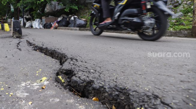 Warga melintas di samping jalan yang amblas di Jalan Inspeksi Kali Ciliwung, Jatinegara, Jakarta Timur, Jumat (4/2/2022). [Suara.com/Alfian Winanto]