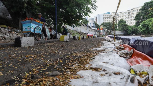 Warga melintas di samping jalan yang amblas di Jalan Inspeksi Kali Ciliwung, Jatinegara, Jakarta Timur, Jumat (4/2/2022). [Suara.com/Alfian Winanto]