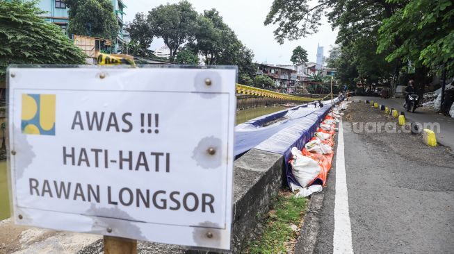 Warga melintas di samping jalan yang amblas di Jalan Inspeksi Kali Ciliwung, Jatinegara, Jakarta Timur, Jumat (4/2/2022). [Suara.com/Alfian Winanto]