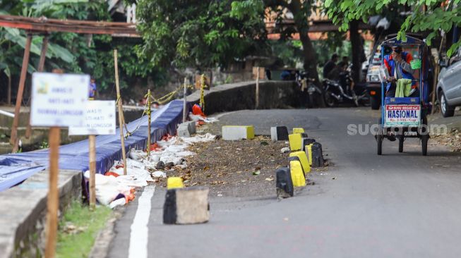 Warga melintas di samping jalan yang amblas di Jalan Inspeksi Kali Ciliwung, Jatinegara, Jakarta Timur, Jumat (4/2/2022). [Suara.com/Alfian Winanto]