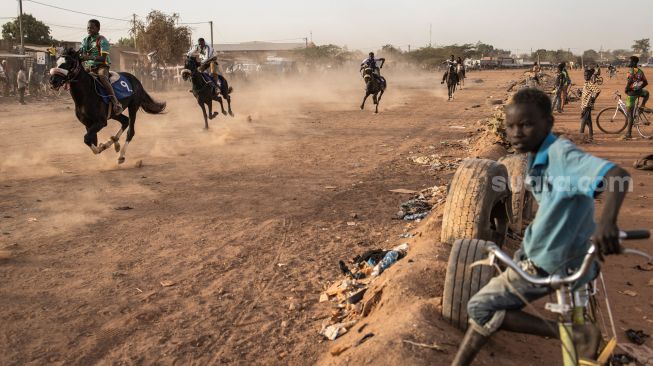 Seorang anak duduk diatas sepedanya saat menyaksikan pertandingan balap kuda di Kota Ouagadougou, Burkina Faso, Senin (30/1/2022). [Photo by JOHN WESSELS / AFP]