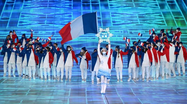 Sambil membawa bendera Perancis, Atlet Tessa Worley and Kevin Rolland memimpin delegasi Perancis saat upacara pembukaan olimpiade musim dingin 2002 di Stadion Bird's Nest, Beijing, China (4/2/2022). [Photo by Manan VATSYAYANA / AFP]