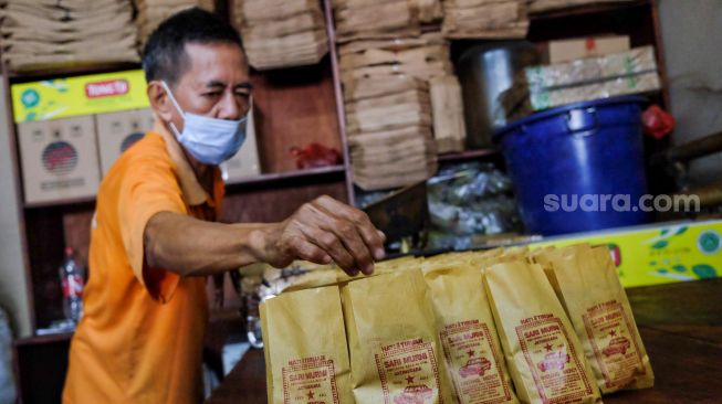 Seorang pekerja memasukan kopi ke bungkusnya di Toko Kopi Sari Murni, Jatinegara, Jakarta Timur, Sabtu (5/2/2022). [Suara.com/Alfian Winanto]