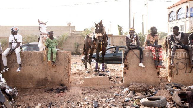 Beberapa pemuda duduk bersama kudanya saat pertandingan balap kuda  di Kota Ouagadougou, Burkina Faso, Selasa (1/2/2022). [Photo by JOHN WESSELS / AFP]