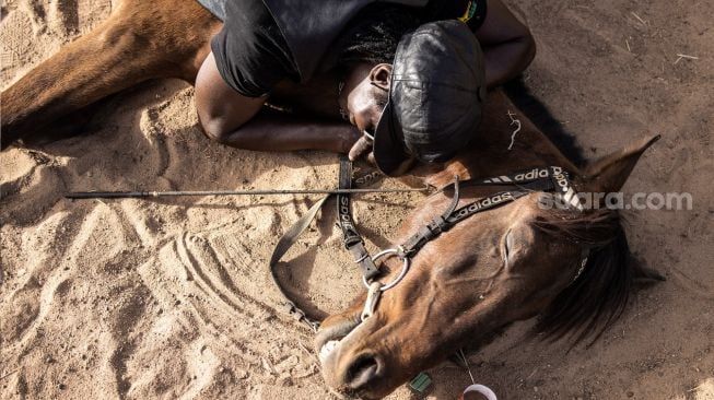 Beberapa pemuda duduk bersama kudanya saat pertandingan balap kuda  di Kota Ouagadougou, Burkina Faso, Selasa (1/2/2022). [Photo by JOHN WESSELS / AFP]