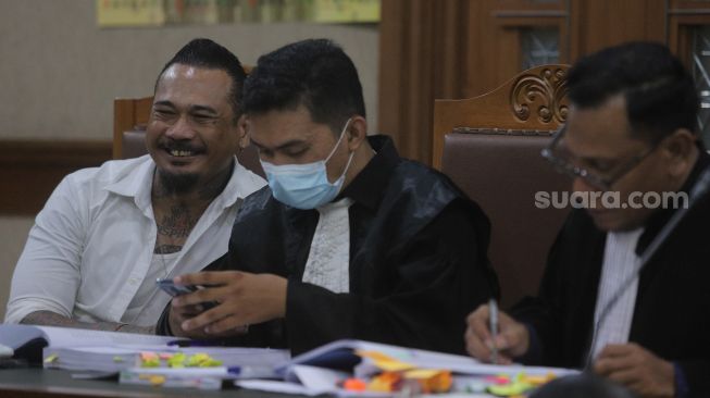 Terdakwa yang juga musisi I Gede Ari Astina atau Jerinx Superman is Dead (SID) (kiri) bersiap menjalani sidang lanjutan kasus pengancaman melalui media elektronik pada Adam Deni dengan agenda mendengarkan keterangan dari saksi ahli di Pengadilan Negeri (PN) Jakarta Pusat, Jakarta, Senin (7/2/2022). [Suara.com/Angga Budhiyanto]