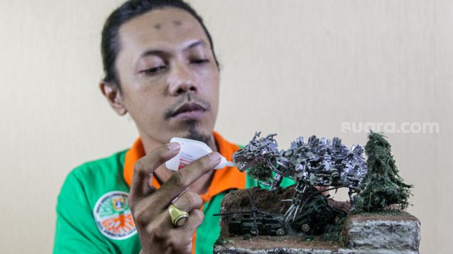 Seto Krisna Putra saat membuat miniatur robot dari limbah korek gas di Pinang Ranti, Jakarta Timur, Kamis (10/2/2022). [Suara.com/Alfian Winanto]