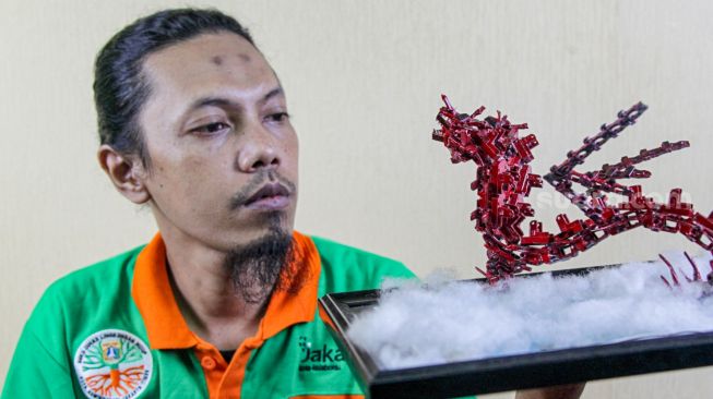 Seto Krisna Putra saat membuat miniatur robot dari limbah korek gas di Pinang Ranti, Jakarta Timur, Kamis (10/2/2022). [Suara.com/Alfian Winanto]