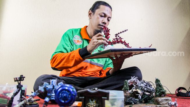 Seto Krisna Putra saat membuat miniatur robot dari limbah korek gas di Pinang Ranti, Jakarta Timur, Kamis (10/2/2022). [Suara.com/Alfian Winanto]