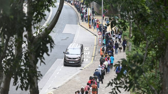 Antrian panjang warga yang mengular hingga ke jalanan untuk mengikuti tes di stasiun pengumpulan spesimen bergerak untuk pengujian Covid-19 di Distrik Tung Chung, Hong Kong, Kamis (10/2/2022). [Peter PARKS / AFP]