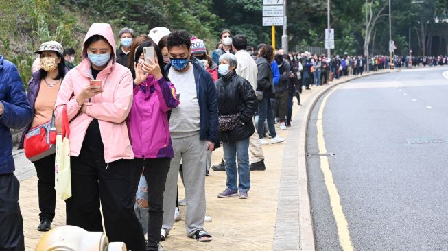 Antrian panjang warga yang mengular hingga ke jalanan untuk mengikuti tes di stasiun pengumpulan spesimen bergerak untuk pengujian Covid-19 di Distrik Tung Chung, Hong Kong, Kamis (10/2/2022). [Peter PARKS / AFP]