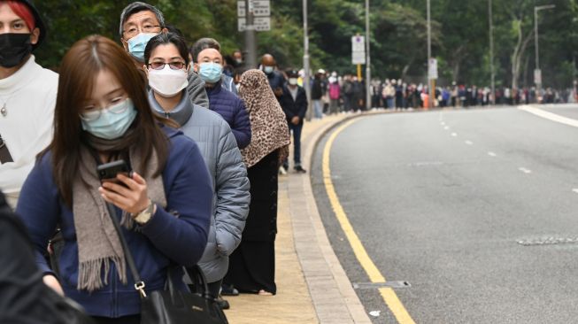 Antrian panjang warga yang mengular hingga ke jalanan untuk mengikuti tes di stasiun pengumpulan spesimen bergerak untuk pengujian Covid-19 di Distrik Tung Chung, Hong Kong, Kamis (10/2/2022). [Peter PARKS / AFP]