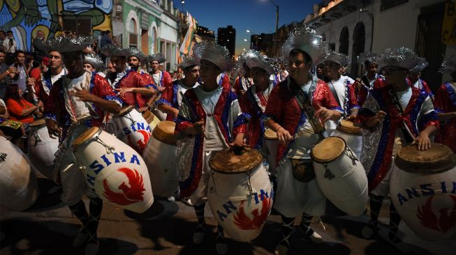 Para penabuh drum yang dikenal sebagai 'komparsa' bersaing dengan memainkan musik dan tarian tradisional 'candombe' saat festival 'Las Llamadas' di Montevideo, Uruguay, Kamis (10/2/2022). [PABLO PORCIUNCULA / AFP]