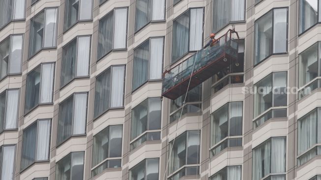 Pekerja membersihkan jendela gedung bertingkat di Kawasan Bundaran Hotel Indonesia (HI), Jakarta Pusat, Sabtu (12/2/2022). [Suara.com/Alfian Winanto]