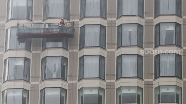 Pekerja membersihkan jendela gedung bertingkat di Kawasan Bundaran Hotel Indonesia (HI), Jakarta Pusat, Sabtu (12/2/2022). [Suara.com/Alfian Winanto]