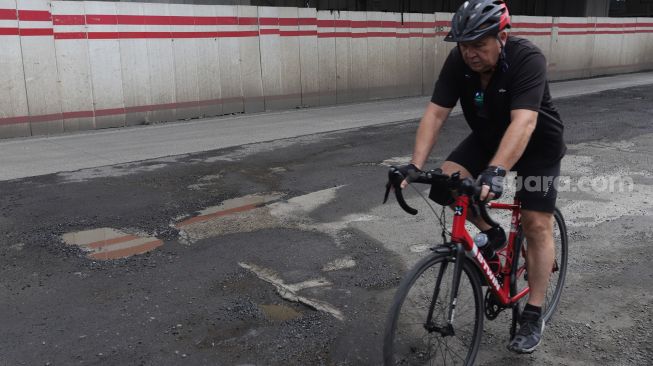 Pesepeda melewati jalan berlubang di Jalan Rasuna Said, Kuningan, Jakarta, Minggu (13/2/2022). [Suara.com/Angga Budhiyanto]