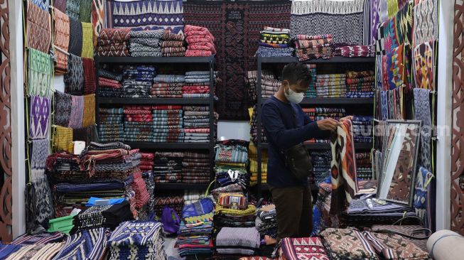 Pramuniaga merapikan kain tradisional saat Pameran Adiwastra Nusantara di Jakarta Convention Center (JCC), Jakarta, Minggu (13/2/2022). [Suara.com/Angga Budhiyanto]